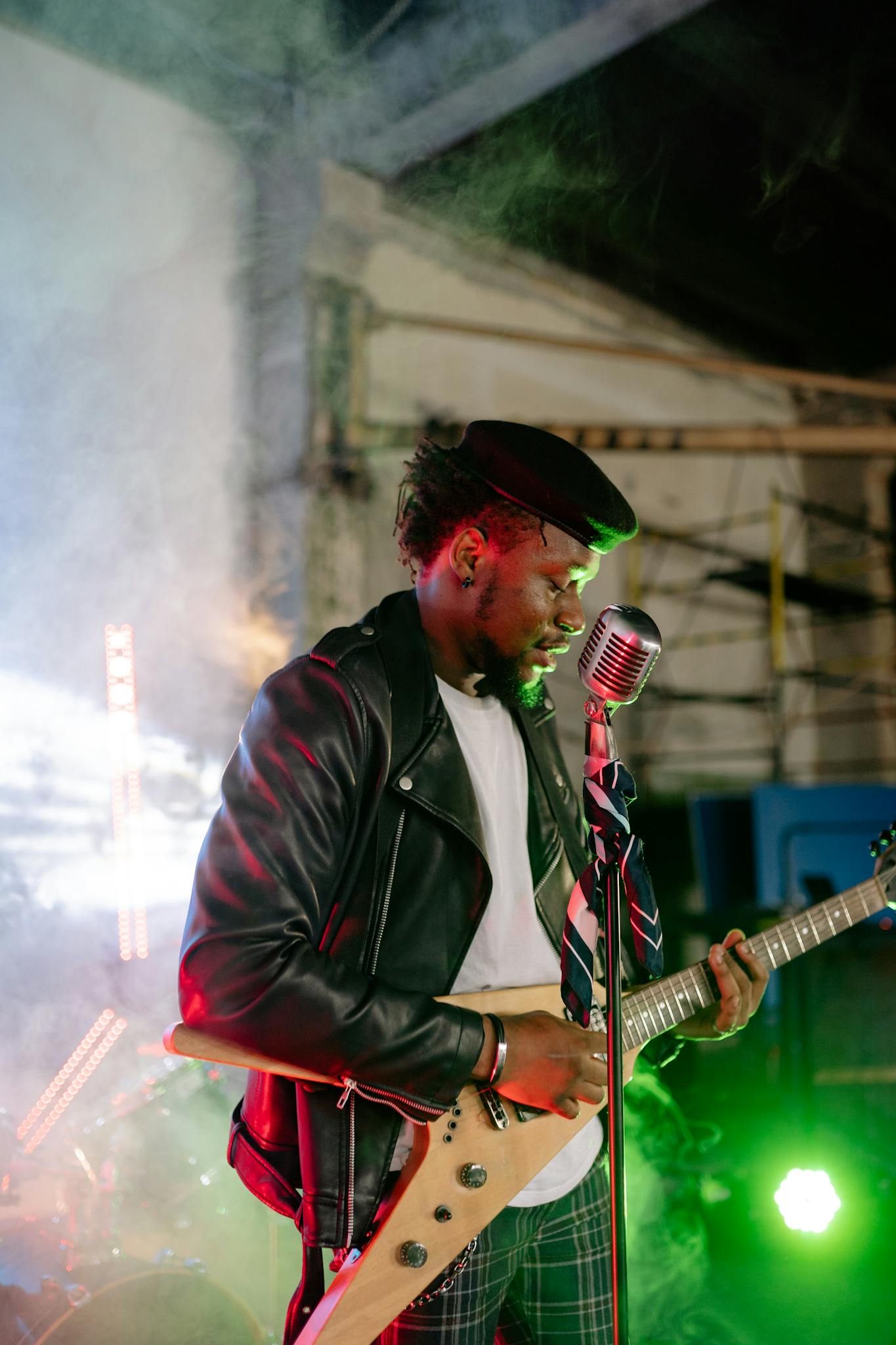 Black musician in leather jacket playing guitar energetically at a night concert.