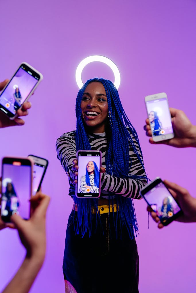 A stylish woman with blue braids surrounded by smartphones capturing her vibrant expression with a halo effect.